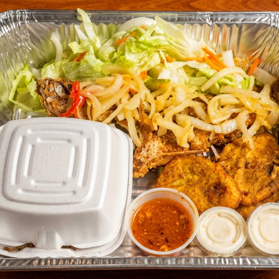 Takeout tray with fried fish, plantains, salad, sautéed onions, and three dipping sauces on a wooden table.