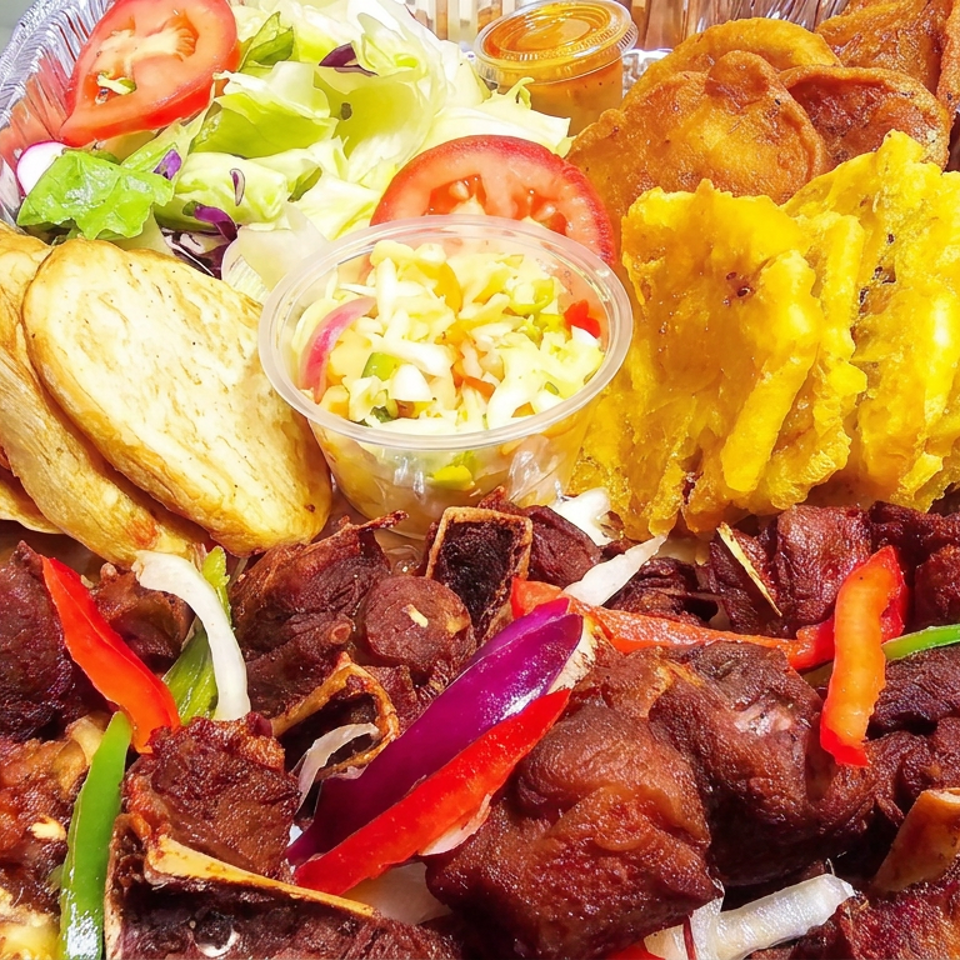 A platter features grilled meat with peppers and onions, fried plantains, salad, toasted bread, a creamy side, and dipping sauce.